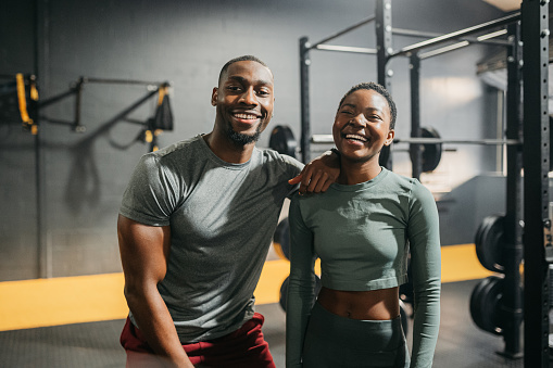 Fitness couple, personal trainer and gym workout with happy man and woman standing together for exercise, training and fit body. Portrait of black accountability partners or friends laughing on break