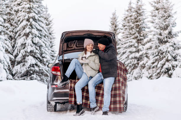 Young couple in love sitting in an embrace in the open trunk of a car,drinking tea in a winter forest.Winter activities,active lifestyle,Valentine's day,tenderness and love stock photo