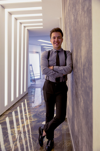 Portrait of happy and smiling businessman with suit arms folded standing in modern office building