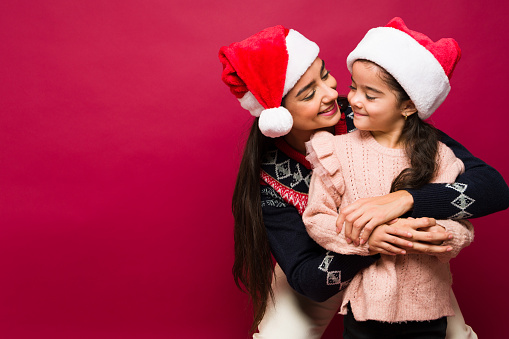 Cheerful mother hugging her adorable little girl celebrating christmas holidays on a red background with copy space