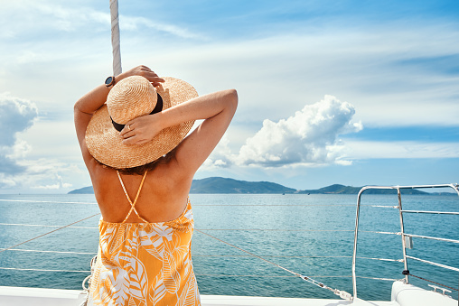 Young elegant woman on edge of yacht looking sea and islands during sailing trip. Happy woman enjoying summer travel on holiday.