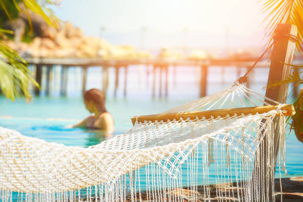 Abstract summer recreation leisure background, closeup hammock with palm leaves, against the backdrop of a resting girl in the pool. Dream vacation, freedom relax travel.