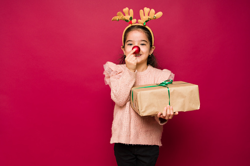 Cute little kid playing with a reindeer nose and costume while enjoying the christmas holidays and presents