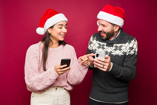 Cheerful couple laughing while texting family and friends for the christmas holidays and using social media