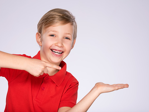 Portrait of cheerful boy pointing to the right -  isolated over white background. 8 year old kid pointing something. Child points by fingers to the side. Cheerful boy in a red t-shirt shows something