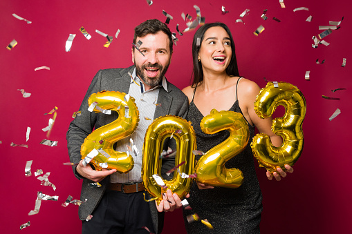 Beautiful couple looking excited celebrating new year's eve 2023 with balloons and confetti