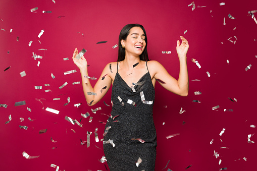 Beautiful excited young woman on a black dress at a new year's eve party laughing while enjoying the confetti