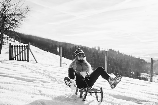 Crazy girl speeding with vintage sledding on snow high mountain - Focus on face - Black and white editing