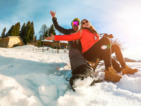 Happy couple having fun with wood vintage sledding on snow high mountains - Focus on girl face