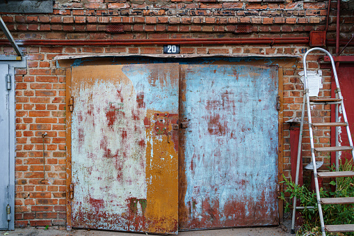 old metal brick garage door with stripped paint and ladder stepladder. the concept of abandoned buildings, painting and repair of buildings.