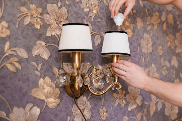 A male electrician changes the light bulbs and repairs in the sconces