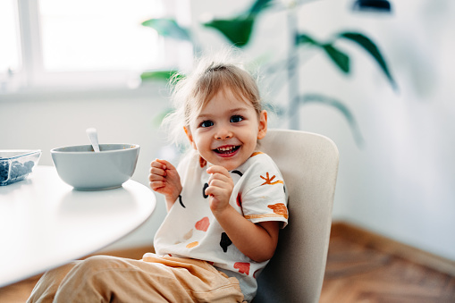 Portrait of smiling girl having fun while eating cereals with fruit for breakfast in the kitchen.
