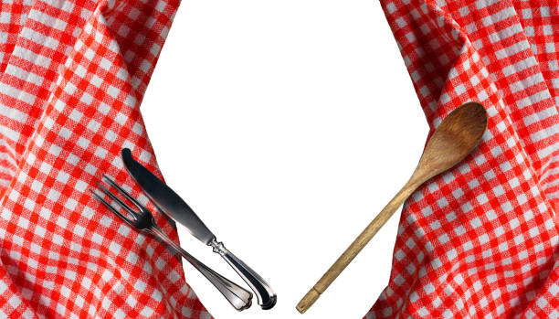 Close-up of a red and white checkered tablecloth with silver cutlery (fork and knife) and wooden spoon, isolated on white background. Directly above, photography.