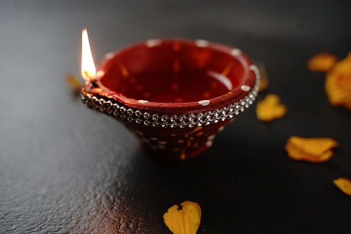 Happy Diwali background - Colorful Clay Diya lit during Deepavali festival on black background, top down view
