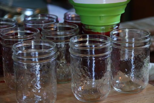 Several 250 ml mason jars placed on cutting board being filled with cooked jam