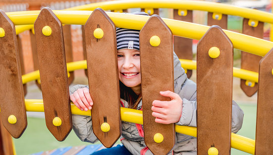 Little smiling girl peeping through a wooden fence on playground