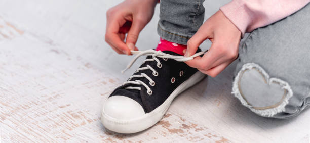 Child tying shoelaces Little girl sitting on the floor and tying shoelaces on her black and white colour snikers child tied up stock pictures, royalty-free photos & images