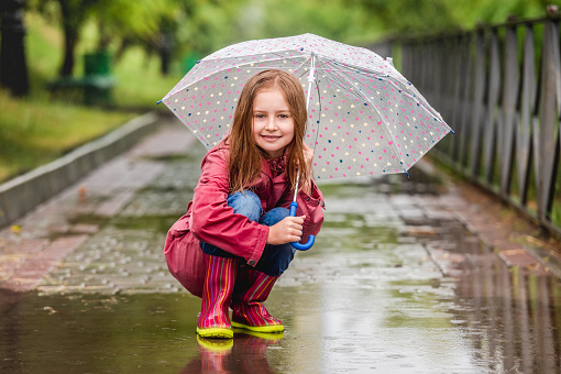 Little girl hiding from rain under umbrella in urban park