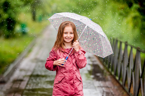 Little girl walking under umbrella and falling raindrops on foreground in spring park