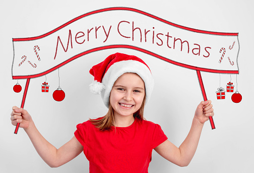Little girl in santa hat holding merry christmas slogan painting on white wall background