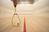Male hand holding a racket inside a squash court. Low angle, unrecognizable person, large depth of field