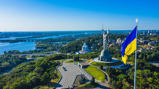 Aerial view to the  Beautiful landscape city Kiev with a Dnepr river. Top view to the Motherland statue in the Kiev. The well-known landmarks in Kyiv. Closeup National flag og Ukraine.