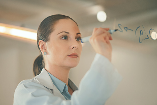 Woman scientist writing molecule on glass, planning particles and math innovation ideas in research laboratory. Poland physics expert, chemical analytics development and test solution notes on window