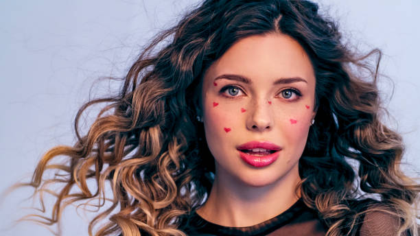 istock Beautiful model with drawn hearts on her cheeks posing in the studio. Fashion model is photographed in a photo studio looking away from the camera. Beautiful young woman with long hair. 1429039000