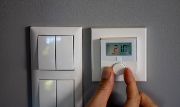 Hand changes the temperature to 21 degrees Celsius on a electronic thermostat. Symbol for saving energy. stock photo
