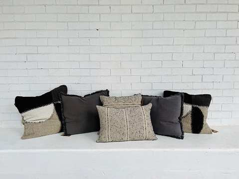 Horizontal closeup photo of a large group of black, grey and beige coloured cushions on display on a white bench against a white painted brick wall in a homewares shop in Byron Bay, NSW.