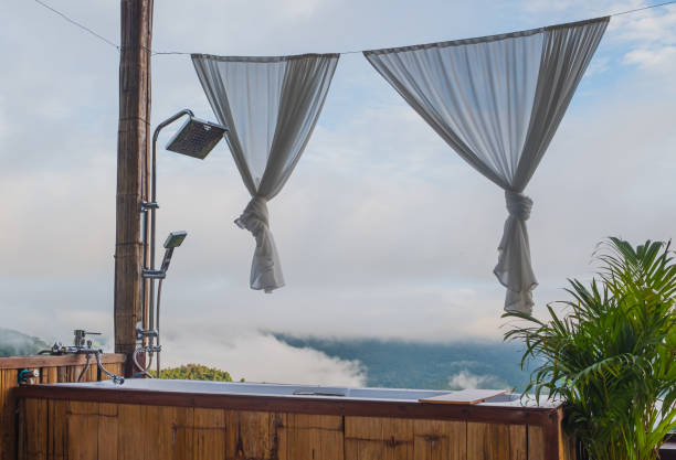 Landscape image of an outdoor white outdoor bath decorated in brown wood with stainless steel faucet and shower. with clouds and mountains in the background The background image is out of focus, stock photo