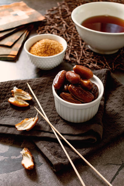 Sweet dried dates in glucose syrup, in a small bowl with long skewers, brown sugar and tea stock photo