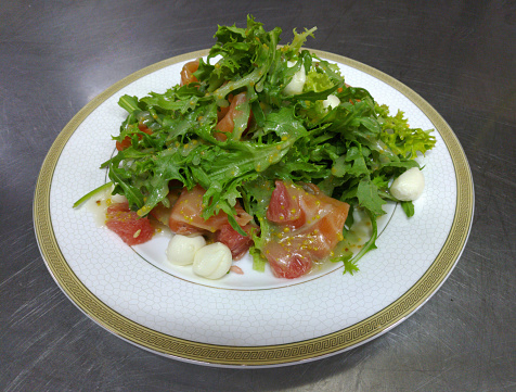light diet salad of salmon, grapefruit and a mix of greens with arugula and mozzarella on a white plate. delicious and healthy food during a diet, for lunch or dinner