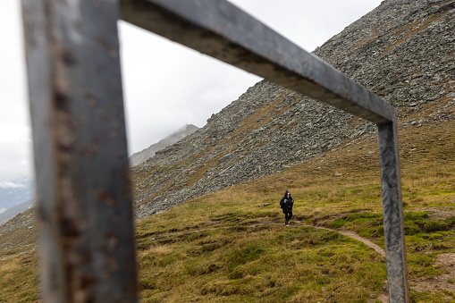 A woman in a rain cape climbs a mountain path, a picture in a metal frame. Austria, Alps. High quality photo