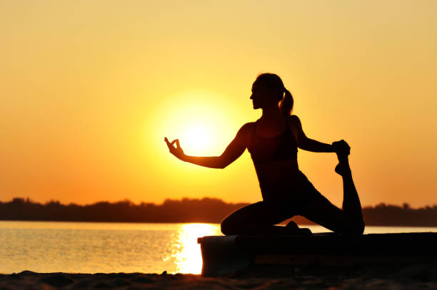 Silhouette of a woman practicing pigeon yoga pose Silhouette of a woman practicing pigeon yoga pose yoga stock pictures, royalty-free photos & images