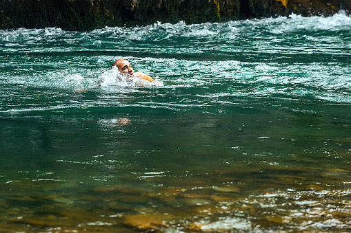 a man actively swims in a cold mountain river with a rapid current on a sunny day. Active sports tourism