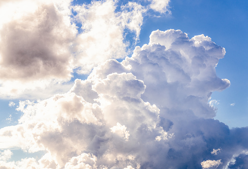 Summer sunlight illuminating a large thundercloud, and smaller surrounding clouds.