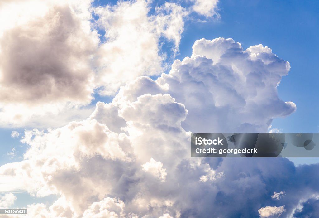 Summer raincloud Summer sunlight illuminating a large thundercloud, and smaller surrounding clouds. Cloud - Sky Stock Photo