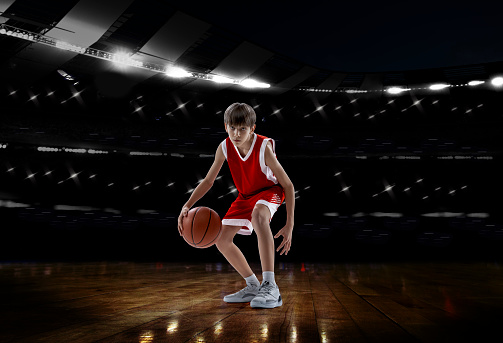 Portrait of teen boy, professional basketball player isolated over sport stadium background. Concentrated sportsman . Concept of sport, active lifestyle, team game, competition. Copy space for ad