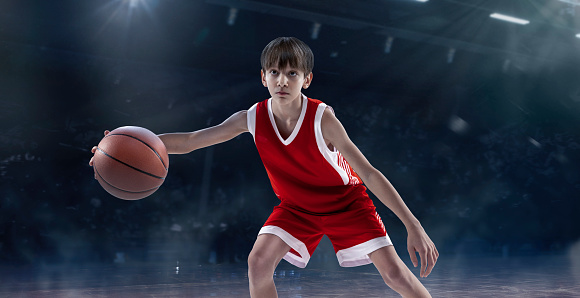 Portrait of teen boy, professional basketball player playing, dribbling isolated over sport stadium background. Concept of sport, active lifestyle, health, team game, competition. Copy space for ad