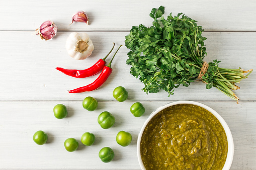 Tkemali sauce, traditional Georgian cuisine, green cherry plum, with ingredients for sauce, cilantro, mint, hot pepper, garlic, on a white wooden table, close-up, rustic, food background, no people, selective focus, sauce, green sauce, tkemali, georgian cuisine, homemade,