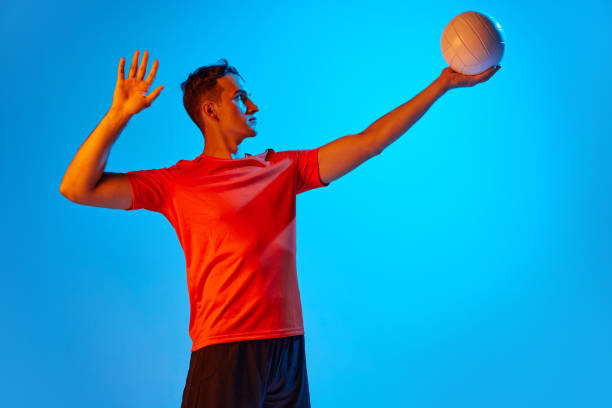 istock One male volleyball player in orange-black uniform training with ball isolated on blue studio background in neon light. Sport, gym, team sport, challenges 1429073757