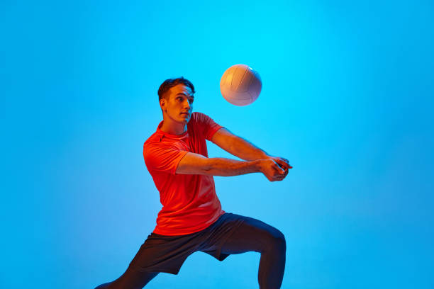 istock One male volleyball player in orange-black uniform training with ball isolated on blue studio background in neon light. Sport, gym, team sport, challenges 1429073774