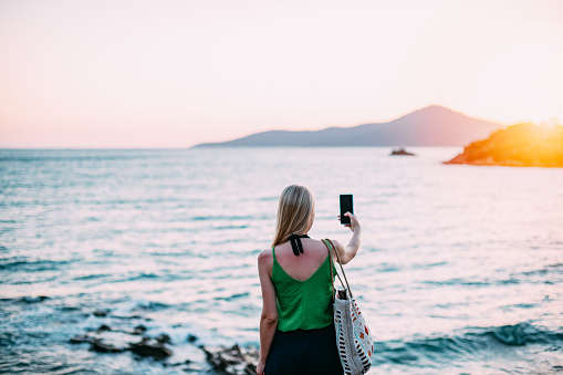 Young Woman Taking Pictures on the Beach at Sunset