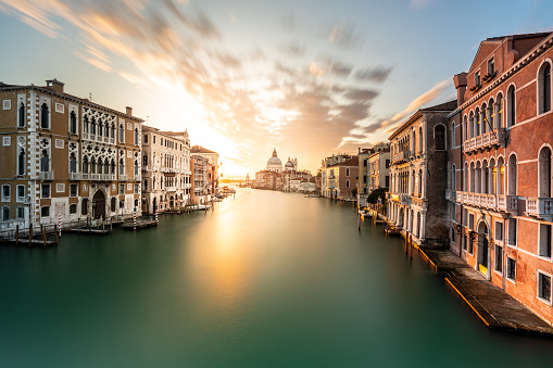 Quiet morning at sunrise in venice, traditional old buildings along water of grand canal, with basilica di santa maria della salute in the back, long exposure