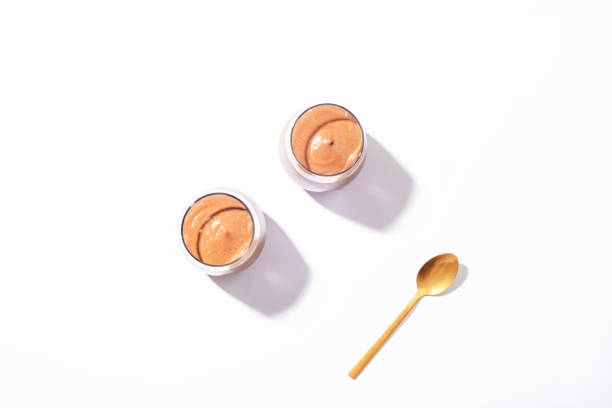istock Two glasses with chocolate mousse and a spoon in sunlight on a white background. Morning breakfast, vegan food. Top view, flat lay 1429075956