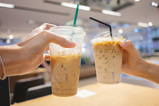 Couple hand holding resueable ready to drink plastic coffee latte cup in cafe