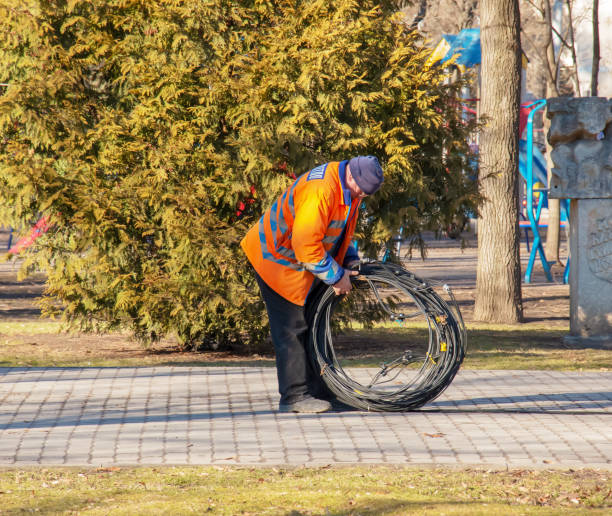 A municipal service worker in an orange uniform carries a coil of cable for further work. stock photo