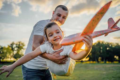 Cheerful father and cute little daughter playing together in the park with toy airplane