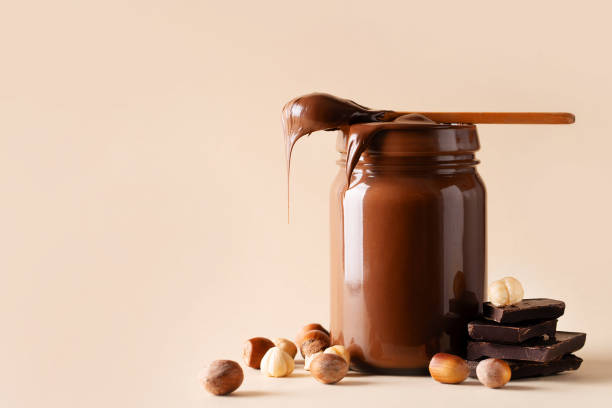 chocolate paste in jar with nuts on cut wooden board - chocolate spread imagens e fotografias de stock
